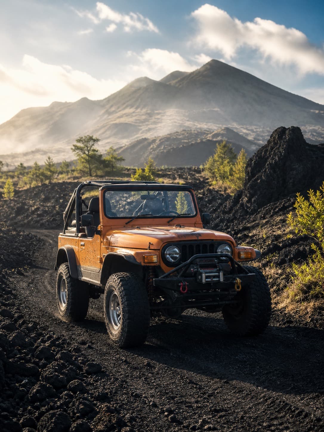 An open-top orange 4x4 on a black lava track, the Batur cone in the haze behind it